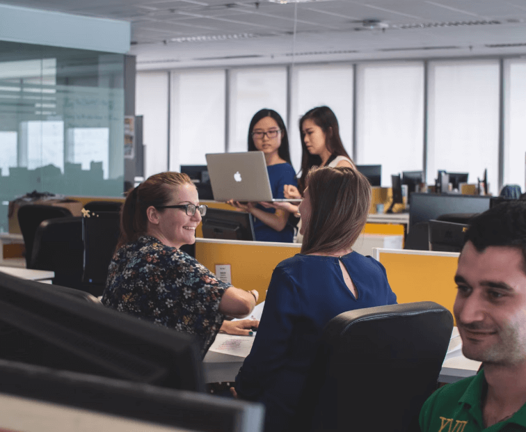 People in an office, talking and being on computers and laptops